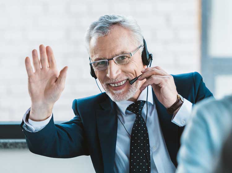 Älterer Herr mit Headset telefoniert mit Kunden und winkt